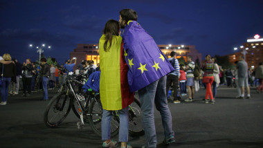 Doi tineri protesteaza in Piata Victoriei infasurati cu drapelul Romaniei si steagul UE