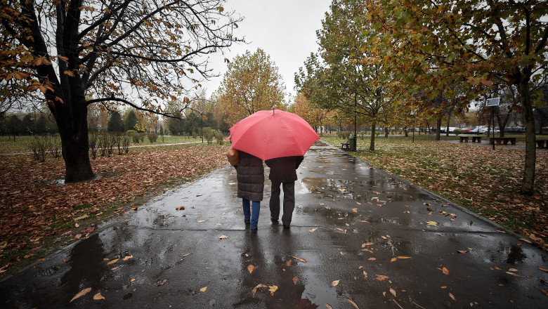 doi oameni merg in parc prin ploaie sub o umbrela rosie