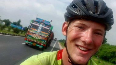 Charlie Condell își face un selfie stând pe bicicletă. În fundal se observă un camion.