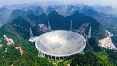 Pesiaj de natură. Un telescop uriaș, de forma unei farfurii, este încadrat de creste de munți, văi și ceață.