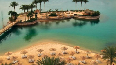 Imagine idilica din statiunea Hurghada. Apa azurie, palmieri, umbrele de stuf in lumina soarelui.