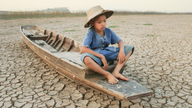 Copil în barcă pe un teren arid. Metaforă a încălzirii globale.