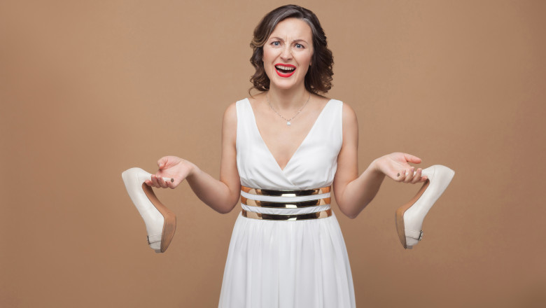 femeie de afaceri imbracata in alb, tinand in maini pantofi inconfortabili cu toc
