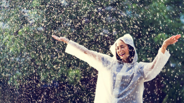 Rainy day asian woman wearing a raincoat outdoors. She is happy.