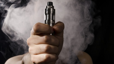holding electronic cigarette with smoke behind.