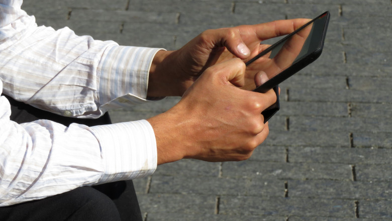 Digital tablet in male hands close-up, man in office suit sitting on the street with tablet PC