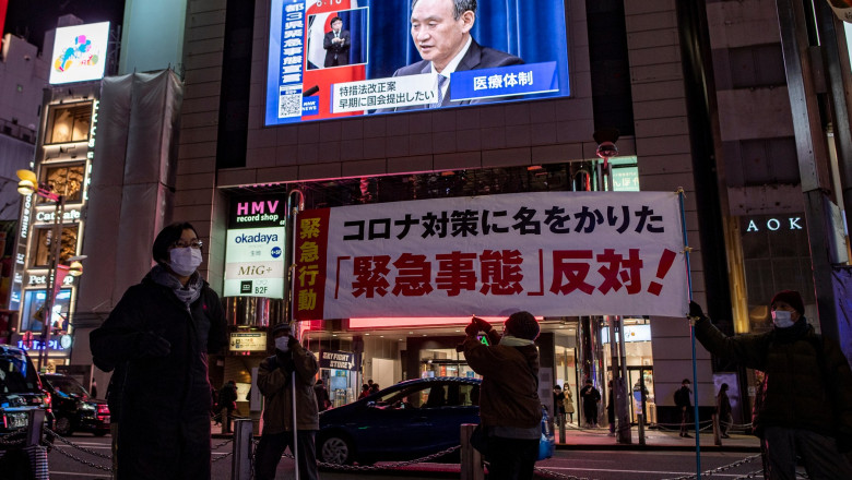 strada din tokyo, cu un panou in care apare premierul japonez anuntand starea de urgenta