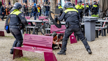 O femeie este ghemuită pe jos în timp ce scutierii intervin pentru a împrăștia la Amsterdam un protest neautorizat împotriva guvernului și a restricțiilor