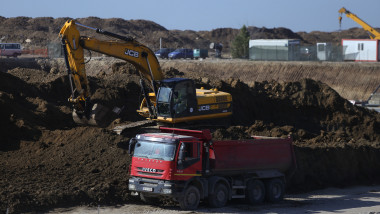 excavator pe maldar de pamant langa un camion pe un santier de constructii