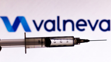 O seringă cu ser fotografiată cu numele și simbolul companiei farmaceutice Valneva pe fundal.