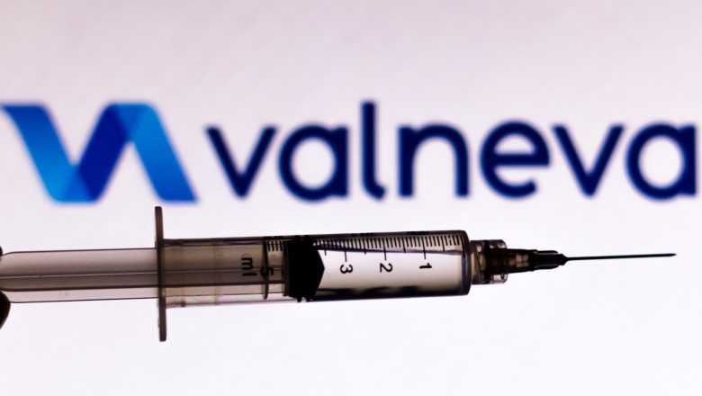 O seringă cu ser fotografiată cu numele și simbolul companiei farmaceutice Valneva pe fundal.