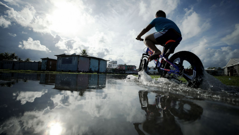 Un tânăr merge cu bicicleta printr-o zonă afectată de maree, în Tuvalu