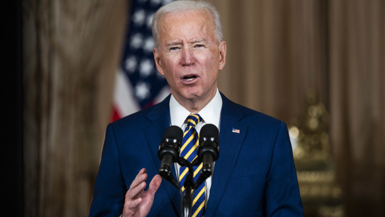 Joe Biden vorbește la pupitru în fața unor microfoane și gesticulează cu mâna stângă.