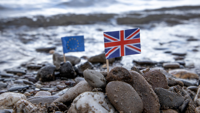 Steaguri în miniatură ale UE și UK pe o plajă, ilustrând conceptul de Brexit