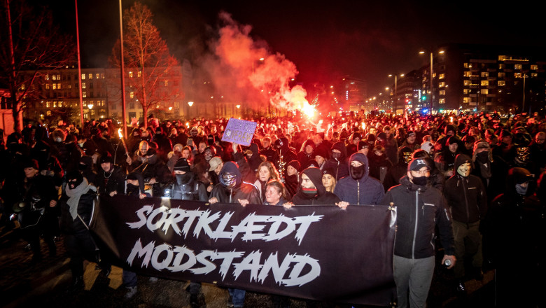 multime de pameni imbracati in negru merg pe strada si tin un banner cu mesaj in daneza