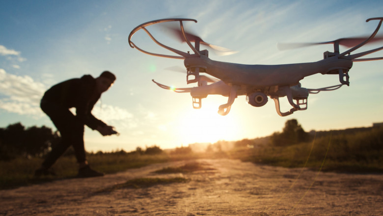 un barbat testeaza o drona la apusul soarelui, pe un camp
