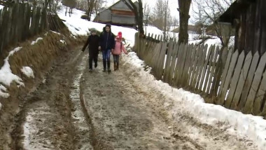 copii care merg pe un drum cu zapada si noroi