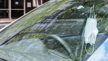 masca de protectie agatata la oglinda unei masini parcate