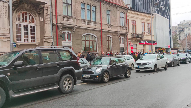 oameni stand la coada, la marginea unui bulevard aglomerat, in Capitala