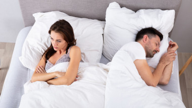 Cuplu în pat, soția supărată, soțul doarme