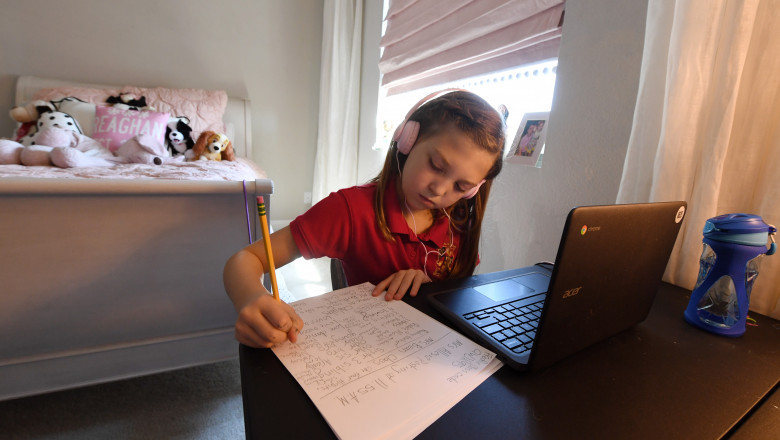 o eleva care face scoala online scrie pe o foaie de hartie, cu un laptop langa ea