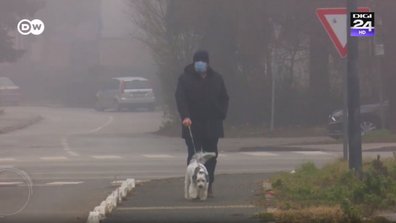 barbat cu masca pe fata care isi plimba cainele in smog