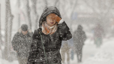 o femeie merge pe strada in bucuresti, in timp ce ninge si bate vantul