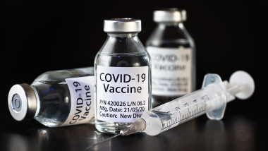 Coronavirus Covid-19 vaccine concept - three glass vials on black table, hypodermic syringe needle near, closeup detail (label own design - dummy data, not real product)