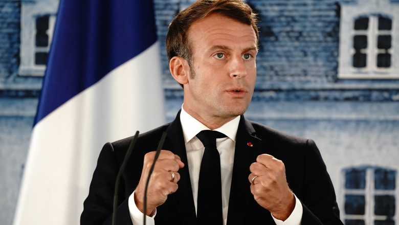 Emmanuel Macron gesticulează cu pumnii strânși în timpul unui discurs cu steagul Franței pe fundal