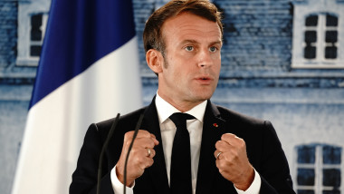 Emmanuel Macron gesticulează cu pumnii strânși în timpul unui discurs cu steagul Franței pe fundal