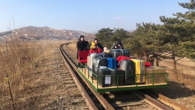 Oameni și bagaje într-un cărucior împins cu mâna pe șine de tren.