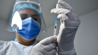 un cadru medical cu viziera si masca extrage o doza de vaccin dintr-o fiola
