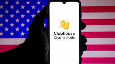telefon cu logoul aplicatiei pentru reteaua sociala clubhouse pe fondul unui steag american