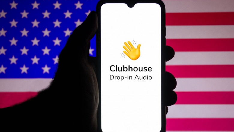 telefon cu logoul aplicatiei pentru reteaua sociala clubhouse pe fondul unui steag american