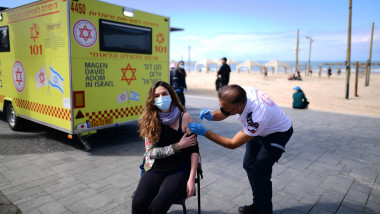 O tânără este vaccinată anti-COVID pe o plajă din Israel.