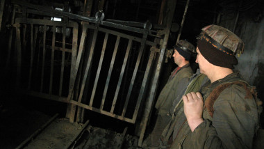 mineri coboara in sut in mina, pe intuneric, cu echipamente de protectie