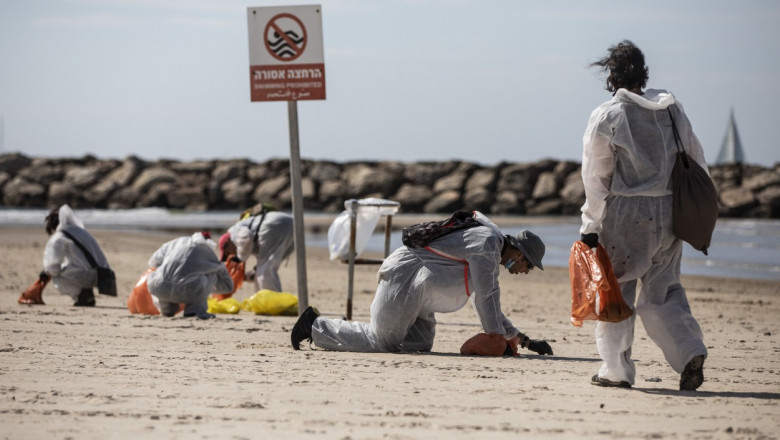 voluntari in haine de protectie culeg gudronul ajuns pe plajele din israel.
