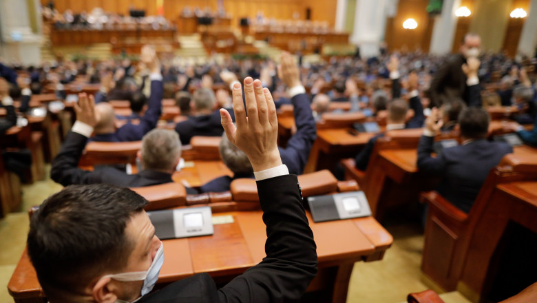 parlamentari care votează cu mâna pe sus în sala de plen