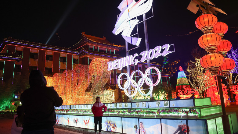 Oameni cu mască în apropiere de un panou luminos de reclamă pentru jocurile olimpice de iarnă din 2022 de la Beijing