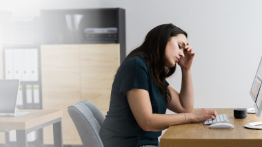 femeie obosită la birou, în fața unui calculator