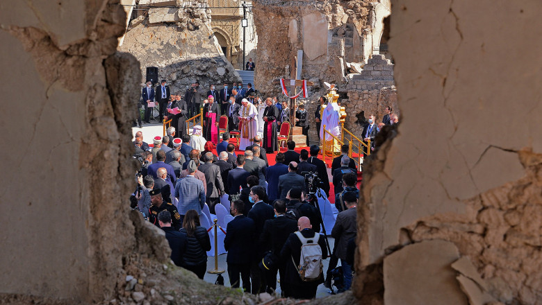Mulțimea adunată în jurul Papei Francisc la Mosul, văzută printr-o spărtură în zid