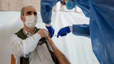 persoana cu masca in timp ce-l vaccineaza o asistenta