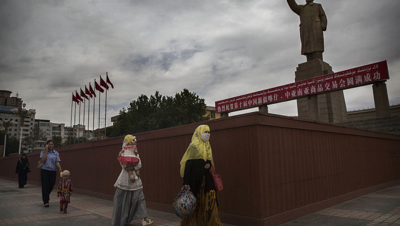 Femei uigure cu văl trec prin dreptul statuii lui Mao, într-un oraș din regiunea Xinjiang, China