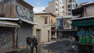 Un bărbat și o femeie trec prin fața unor magazine închise, în Atena.