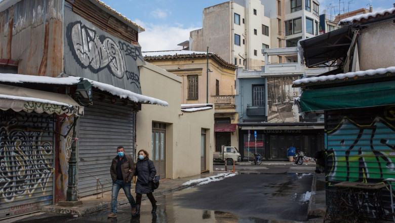 Un bărbat și o femeie trec prin fața unor magazine închise, în Atena.