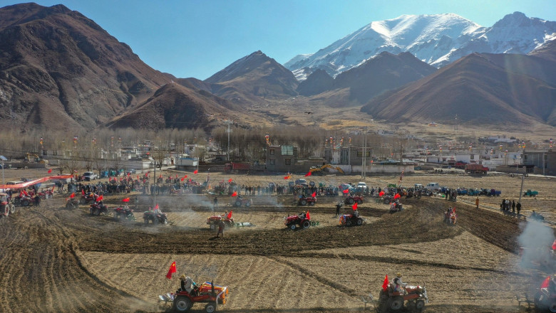 tractoare ara campul in zare se vede orasul lhasa din tibet si muntii himalaya pe fundal