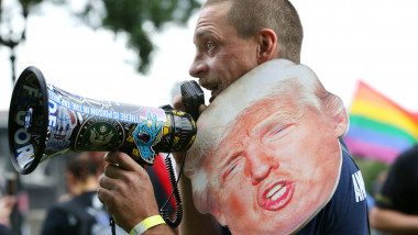 Bărbat care vorbește la un megafon și poartă un carton cu fața fostului președinte Trump pe umăr