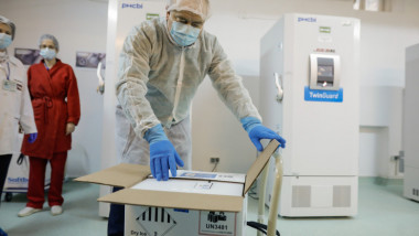 cutie cu doze de vaccin desfacuta de o persoana cu echipament