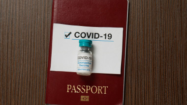 Ilustrație pașaport cu o doză de vaccin deasupra și un bilețel pe care scrie COVID-19