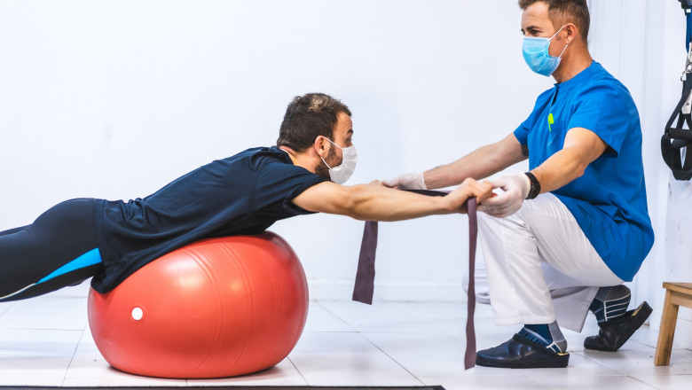 Physiotherapist with mask and a patient doing exercises with a rubber. Physiotherapy with protective measures for the Coronavirus pandemic, COVID-19. Osteopathy, sports chiromassage